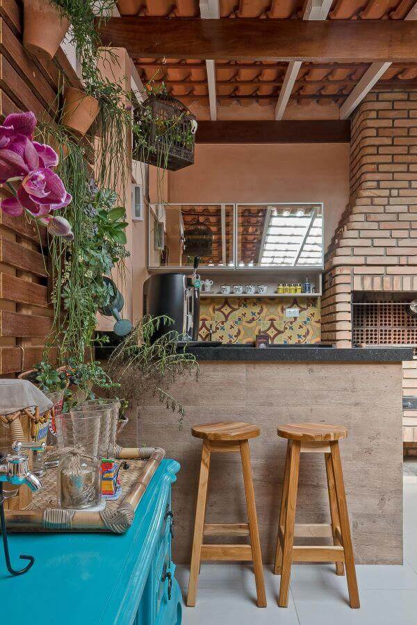 Área gourmet com churrasqueira pequena de tijolinho e jardim vertical perto da mesa azul