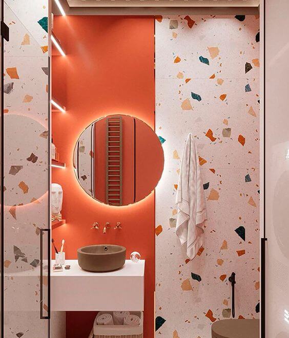Banheiro retrô na cor coral com granilite de revestimento e espelho redondo com led