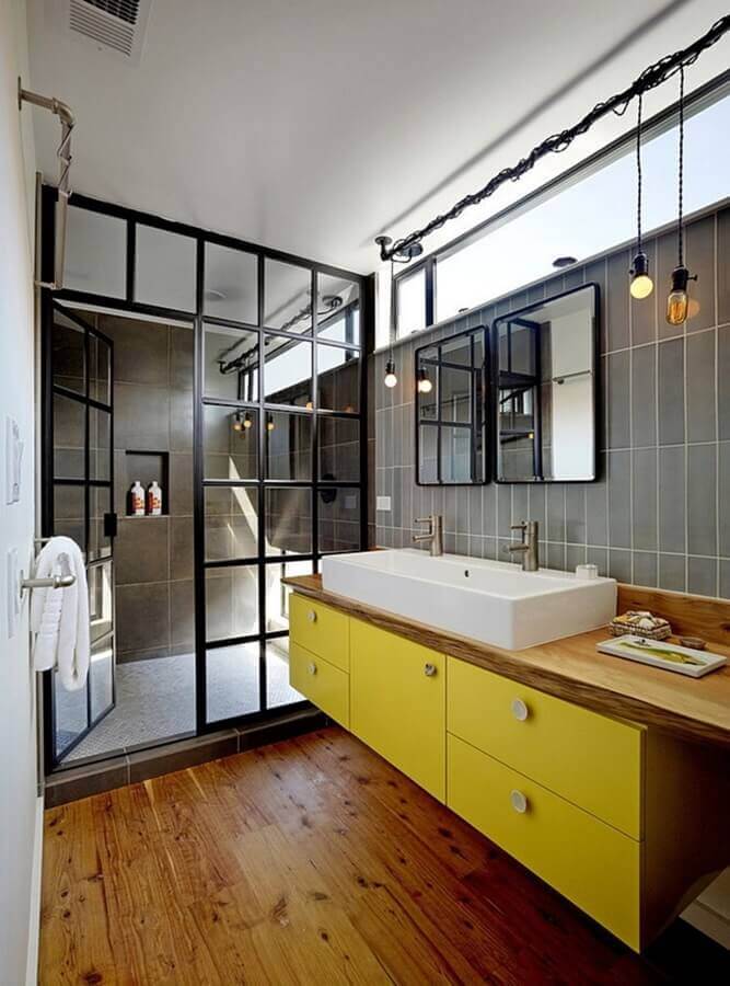 Banheiro industrial decorado com gabinete amarelo e bancada de madeira Foto Robert Nebolon Architects