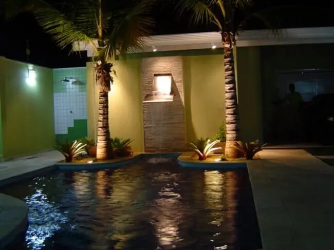 A iluminação destaca a presença das pedras para cascata de piscina.