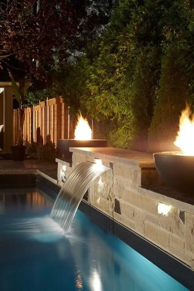 A iluminação externa deve se conectar com a cascata para piscina feita de pedra.
