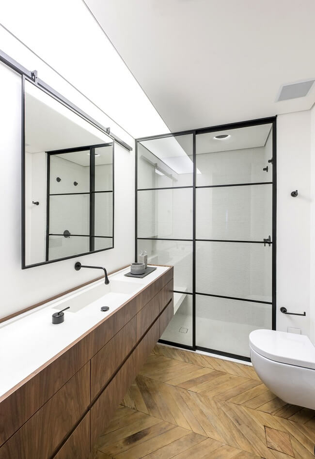 Banheiro feminino minimalista com gabinete de madeira e box com vidro canelado